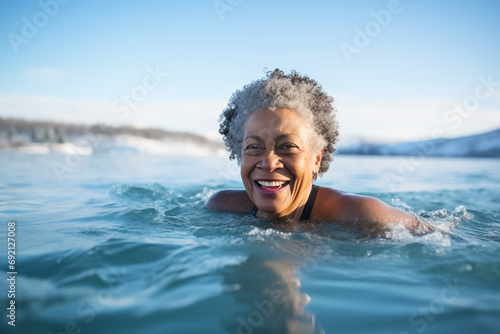 Happy African American active senior woman swimming in ice water in winter outdoors © colnihko