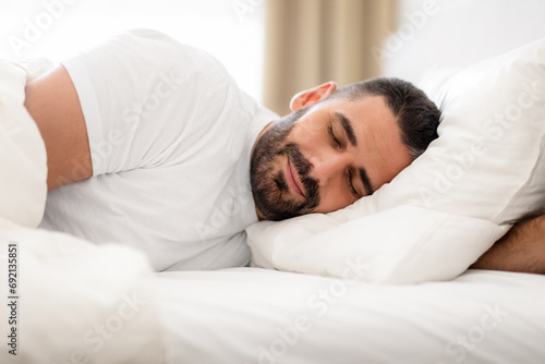 Peaceful millennial man deeply asleep napping in domestic bedroom