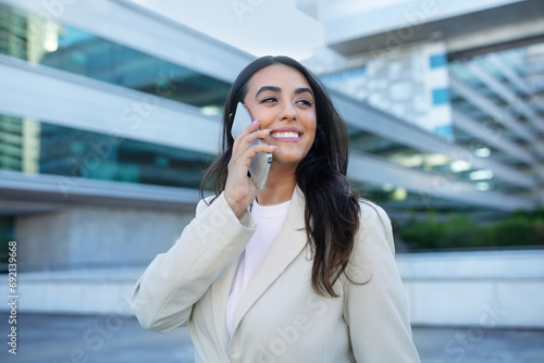 Happy latin entrepreneur woman talking on smartphone outside