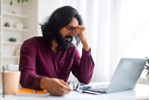 Tired Indian Freelancer Suffering Eyes Fatigue While Working With Laptop At Home © Prostock-studio