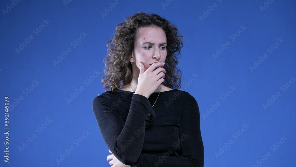 Pensive woman thinking deeply with hand in chin pondering solution to problem. Thoughful preoccupied person on blue background Pensive woman thinking deeply with hand in chin pondering solution to problem. Thoughful preoccupied person on blue background