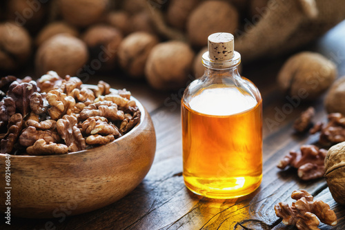 Wooden bowl of walnuts and bottle of essential nut oil on kitchen table.