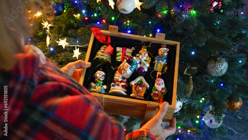 woman's hands holding wooden box with vintage Christmas ornaments with christmas tree on background. 