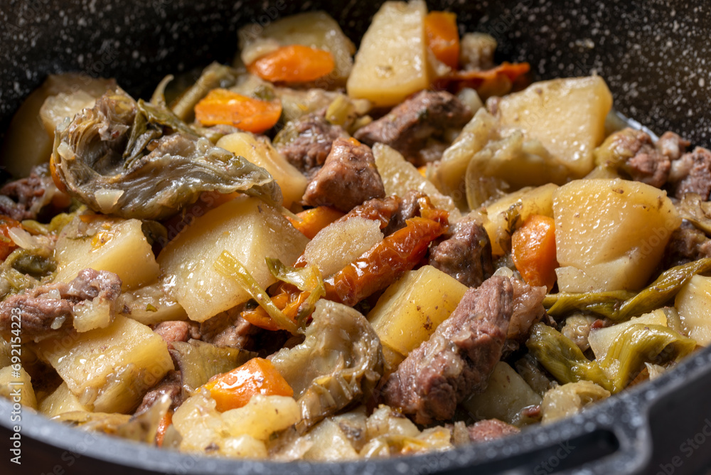 Delizioso spezzatino con carne di maiale, patate, carote, pomodori secchi e carciofi, cibo italiano 
