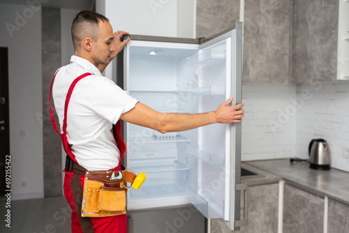 Foto Happy adult handyman repairing refrigerator in domestic kitchen