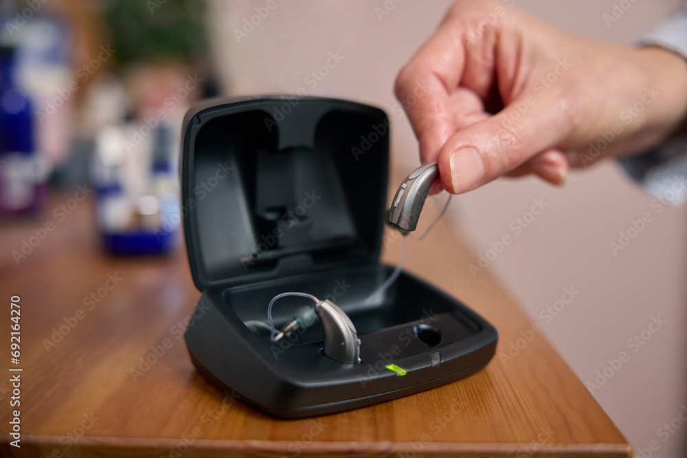 Fototapeta premium Close Up Of Person Picking Up Wireless Hearing Aid Or Device From Charging Case At Home