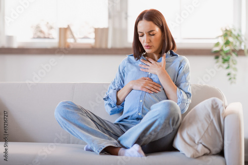 Pregnant lady feeling bad touching tummy and chest at home photo