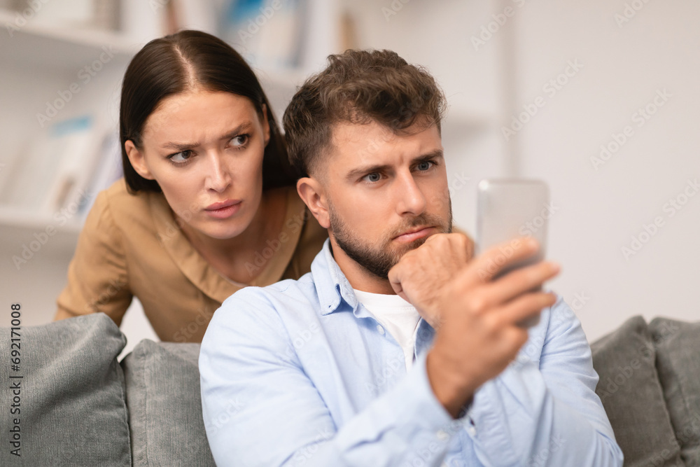 Distrustful young woman sneakily checks her boyfriend's phone at home Distrustful young woman sneakily checks her boyfriend's phone at home