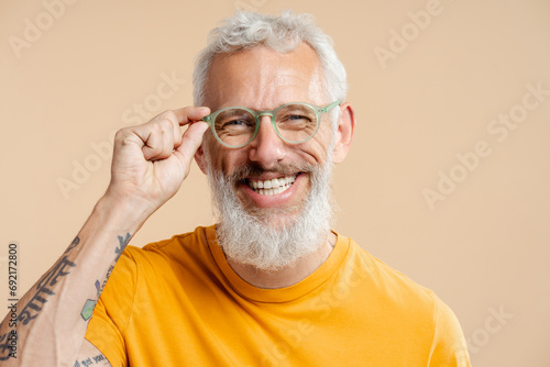 Successful mature man, wearing stylish eyeglasses and yellow t shirt, isolated on beige background