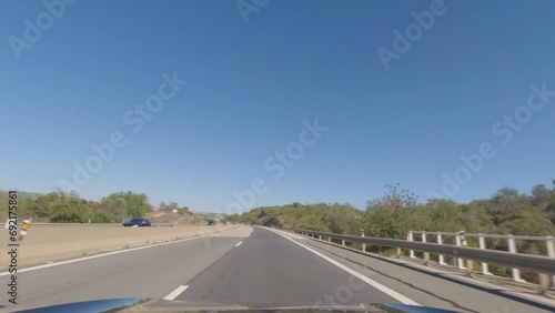 First person view, FPV, from dashcam of car driving along the Algarve Coast in Portugal, driving on the highway towards Faro. Road trip video in POV, with blue sky	 photo