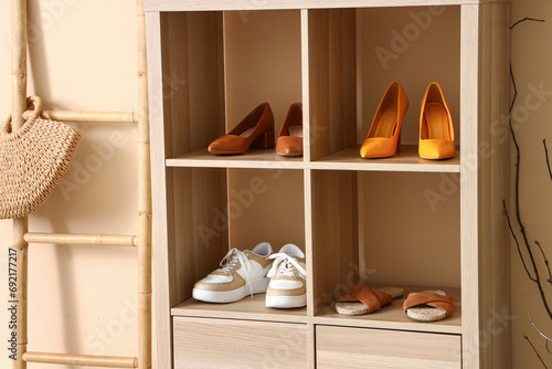 Shelving unit with different stylish shoes and ladder near beige wall in boutique