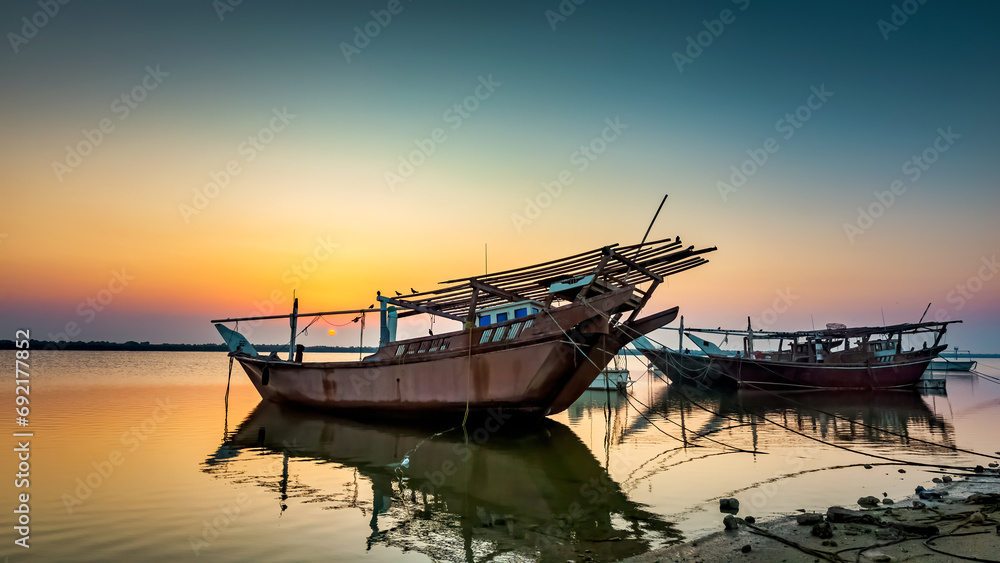 Golden hues paint the tranquil Dammam seaside as boats rest against the morning glow, a serene embrace of nature's beauty in Saudi Arabia.