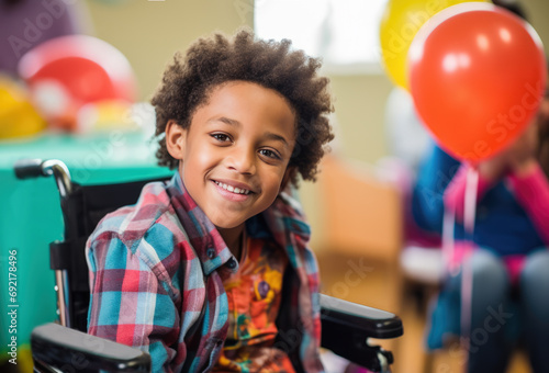 Portrait of a cute young disabled black boy sitting in a wheelchair at a birthday party. Smiling at the camera. 