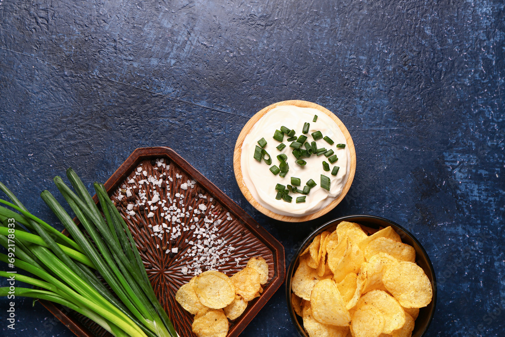 Bowl of tasty sour cream with sliced green onion and potato chips on blue background Bowl of tasty sour cream with sliced green onion and potato chips on blue background