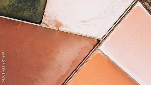 Aerial top down view of saltern evaporation ponds or saltworks evaporation fields under sun for extracting sea salt