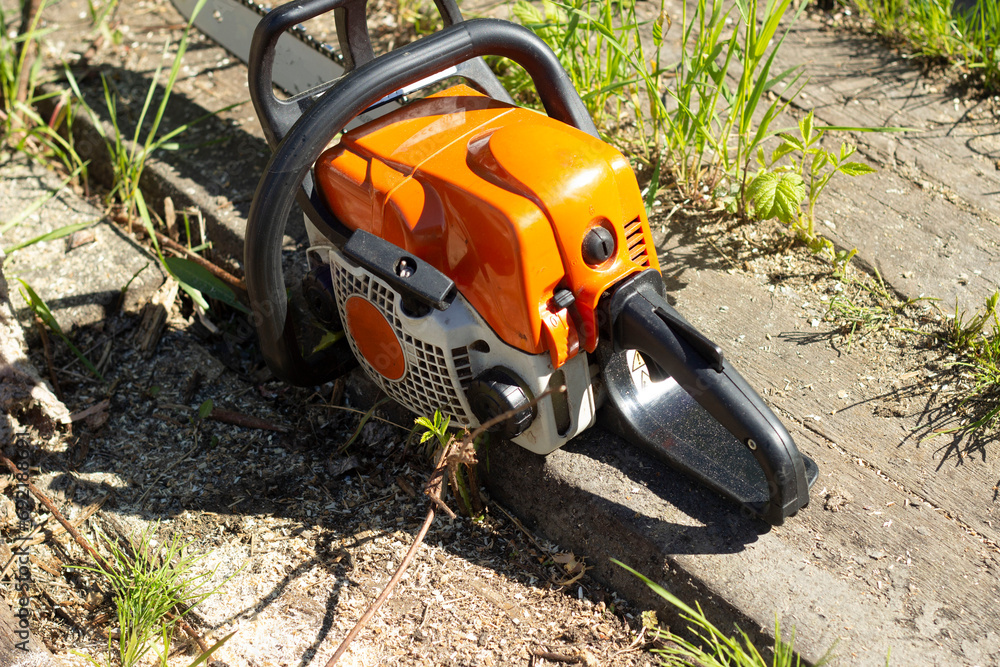an orange chainsaw on the territory of a country house, used for sawing firewood