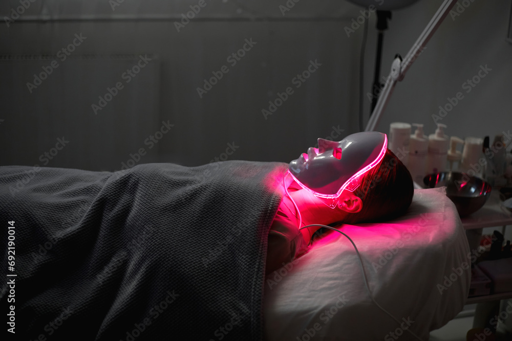Woman getting cosmetic procedure with LED facial mask. , photon therapy - obrazy, fototapety, plakaty 