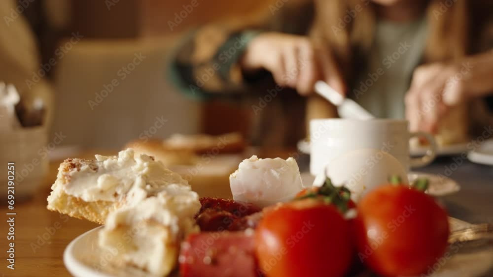 Breakfast in a restaurant with a woman. Rolls spread with cream cheese and tomatoes with eggs on a plate. Close-up. Breakfast in a restaurant with a woman. Rolls spread with cream cheese and tomatoes with eggs on a plate. Close-up.