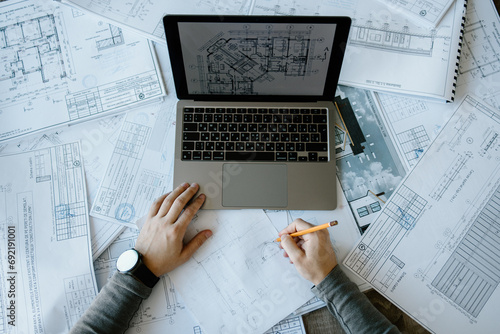 An arhitect working in his office, on his laptop and using a pen, designing a new project. photo