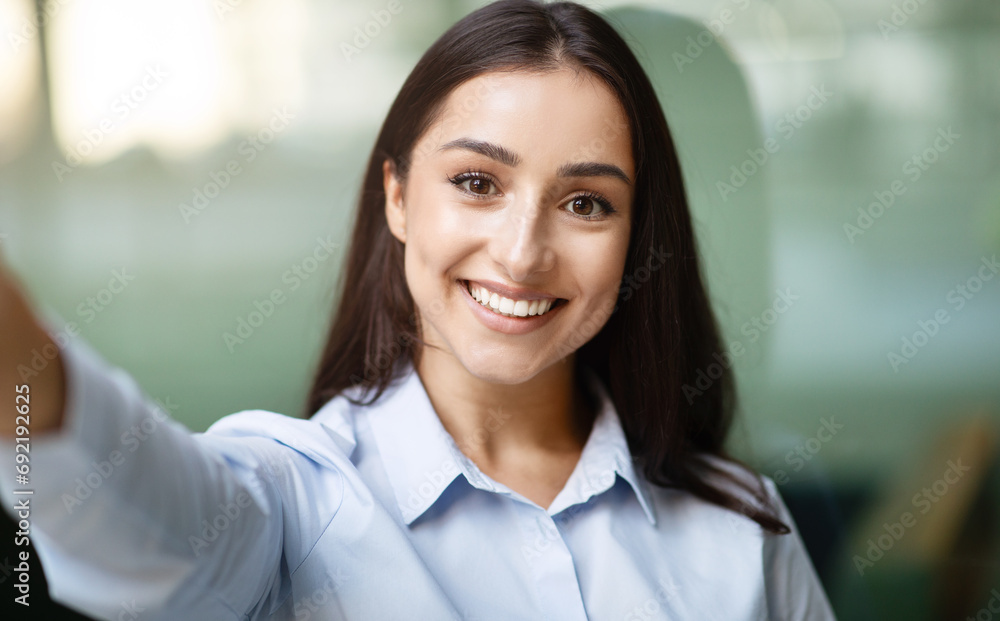 Glad arab young businesswoman with friendly smile take selfie, in modern office building Glad arab young businesswoman with friendly smile take selfie, in modern office building