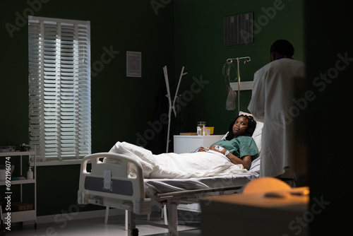 African patient lies in the hospital room as the doctor discusses her treatment.