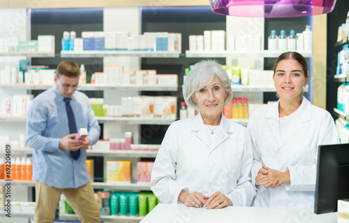 Senior woman and girl pharmacists are standing in pharmacys sales hall, pharmacy staff are amicably preparing to meet chemist shop visitors