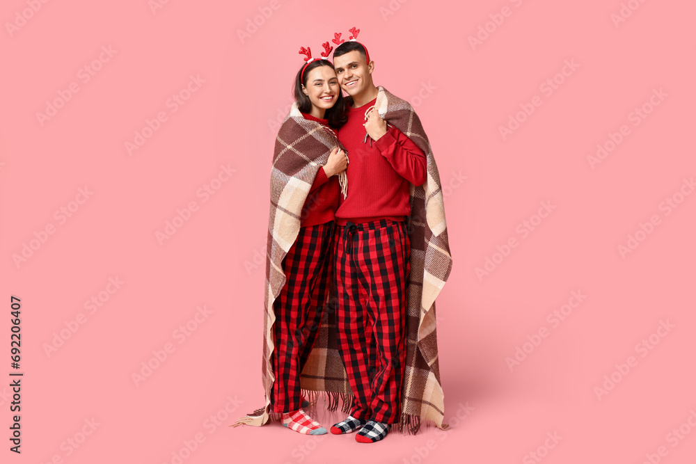 Happy young couple in Christmas pajamas and with plaid  hugging against pink background