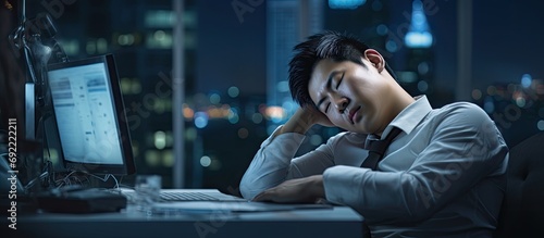 Asian young tired staff officer man using desktop computer having overwork project overnight in office exhausted unhappy businessman feeling sleepy after after working hard overtime at night