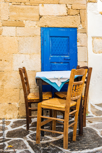 Three wooden chairs and table of a Greek restaurant tavern in narrow street of Plaka village, Milos island, Cyclades, Greece.