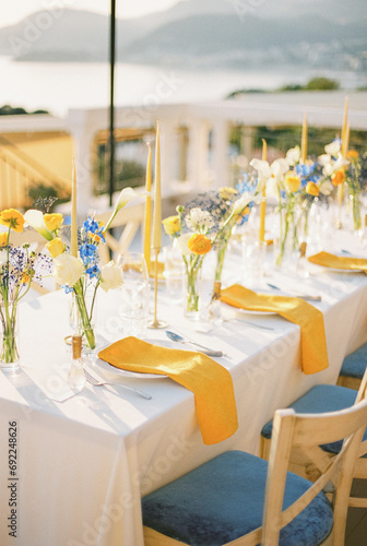 Long festive table with bouquets of flowers and yellow napkins on plates