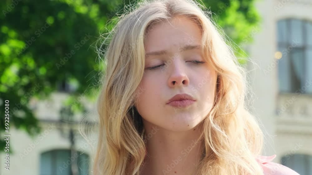 Confused young woman with long blonde hair stands near college. Blonde lady frowns talking about student chores with friend against university Confused young woman with long blonde hair stands near college. Blonde lady frowns talking about student chores with friend against university