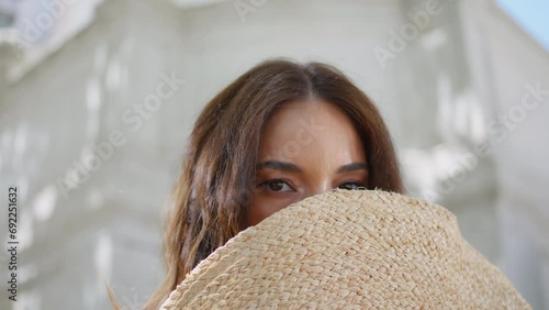 Playful woman hiding face straw hat city portrait. Elegant lady looking camera photo