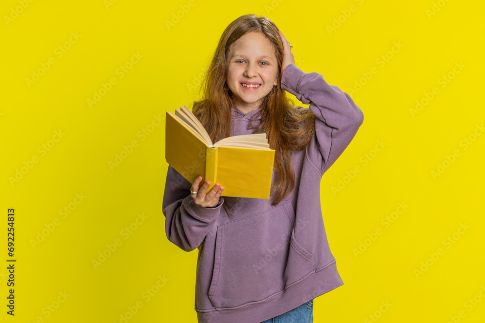 Happy relaxed smiling preteen child girl kid reading funny interesting fairytale story book, leisure hobby, knowledge wisdom, education, learning, study, wow. Children isolated on yellow background Happy relaxed smiling preteen child girl kid reading funny interesting fairytale story book, leisure hobby, knowledge wisdom, education, learning, study, wow. Children isolated on yellow background