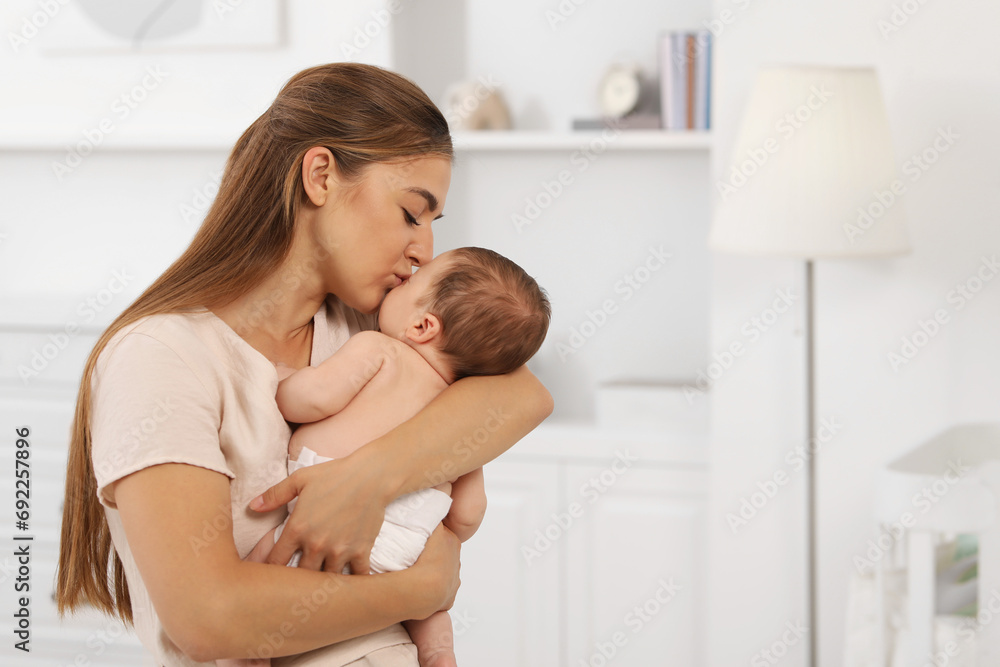 Mother kissing her cute newborn baby indoors, space for text Mother kissing her cute newborn baby indoors, space for text