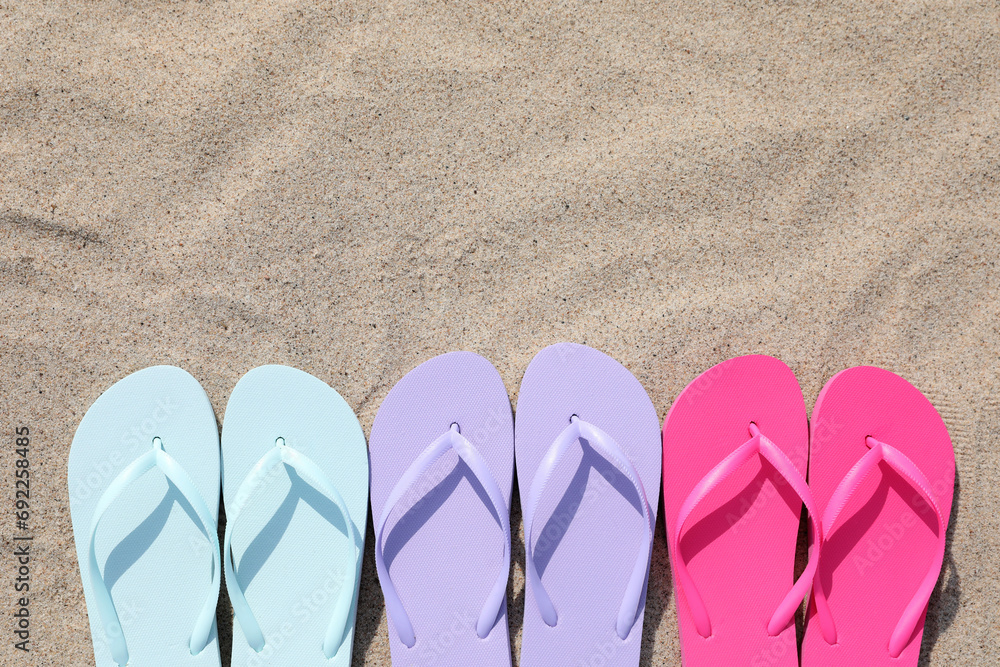 Naklejka premium Stylish colorful flip flops on sand outdoors, flat lay. Space for text