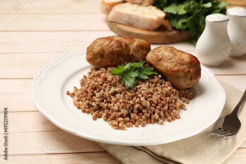 Tasty buckwheat with fresh parsley, cutlets and fork on wooden table, closeup