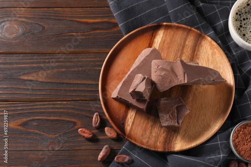 Pieces of tasty milk chocolate, cocoa beans and powder on wooden table, flat lay. Space for text
