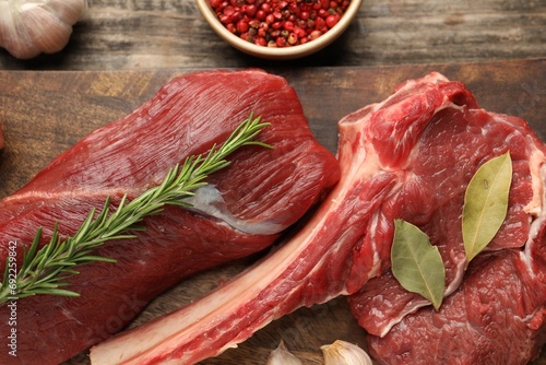 Pieces of raw beef meat and spices on wooden table, flat lay photo