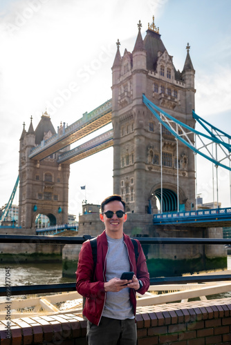 Canvas Print Happy young Latin man wearing sunglasses and red jacket with backpack using smar