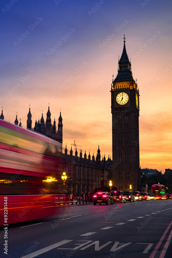 Public transportation bus and cars on asphalt road near Big Ben or Clock Tower under picturesque sky in dusk in London city at night