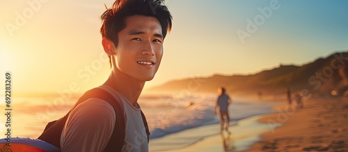 Asian male model in his 20s, surfing with a surfboard at sunset beach, embracing the adventurous lifestyle of outdoor water sports in summer. © AkuAku