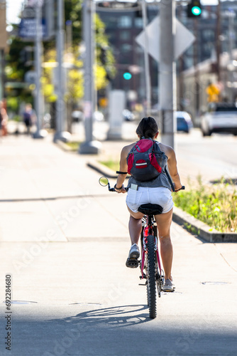 Slender fit girl with a casual backpack and with a mobile phone in her pocket rides a bicycle to keep fit and do daily exercise along the street of an eco-friendly urban city