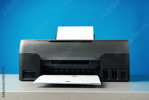 Laser printer on desk against blue background.