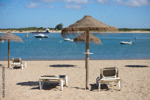 Straw umbrellas and sun loungers on the beach on a sunny day. The concept of rest and relaxation  holidays and travel. In the background the fishermen s boats.