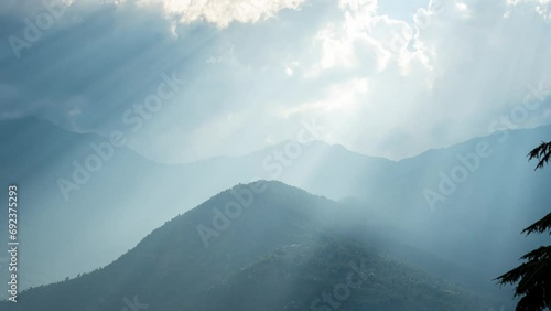 Zoom in 4K time lapse of  sun god rays shining through clouds on mountains in Manali, India. Time lapse of clouds moving over mountains. Dramatic sunrays through the clouds. Sun burst over mountains photo