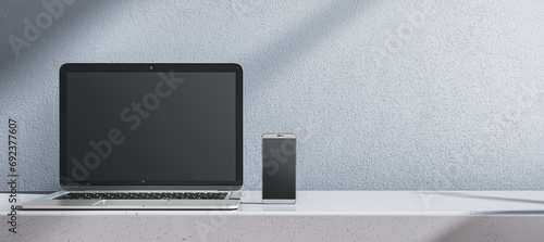 Close up of empty laptop and cellphone on gray desk. Concrete wall background. Device presentation and online education concept. Mock up, 3D Rendering.