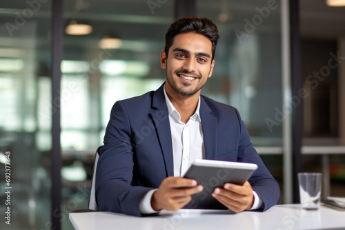 Obraz na płótnie happy young Indian businessman employee manager using a tablet computer, looking at the camera at his office desk w salonie