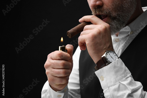Man lighting cigar on black background, closeup. Space for text