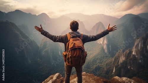 Rear view portrait of young man traveler with backpack standing on a mountain with arms spread open photo