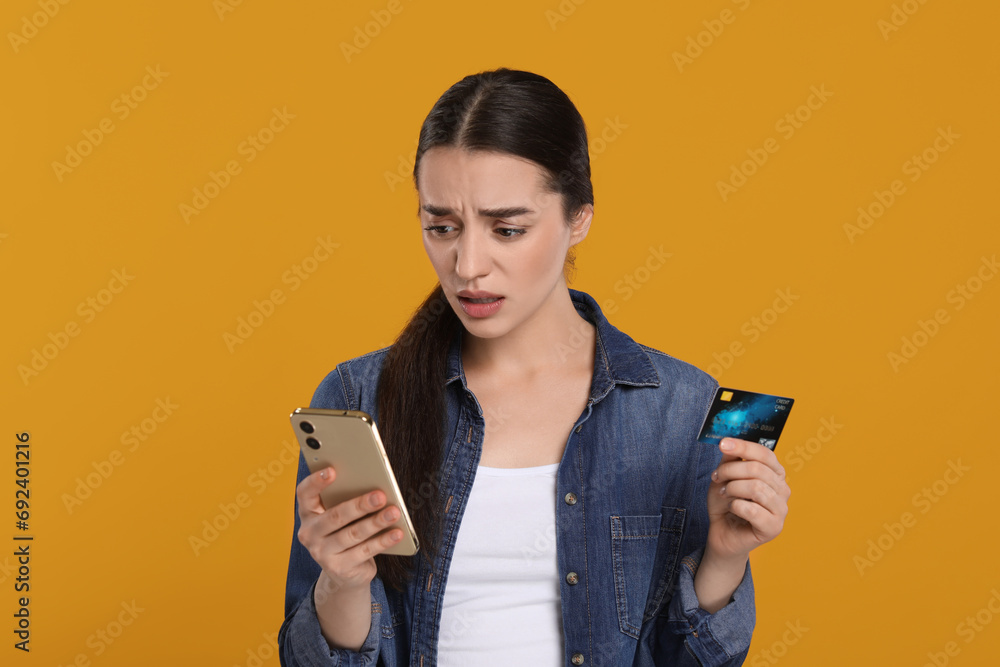 Confused woman with credit card and smartphone on orange background. Debt problem Confused woman with credit card and smartphone on orange background. Debt problem